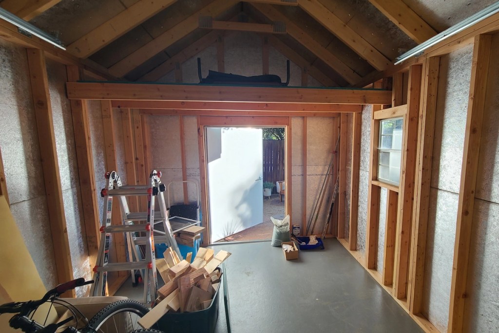 Interior of a backyard shed showing framed walls and open ceiling before electrical rough-in