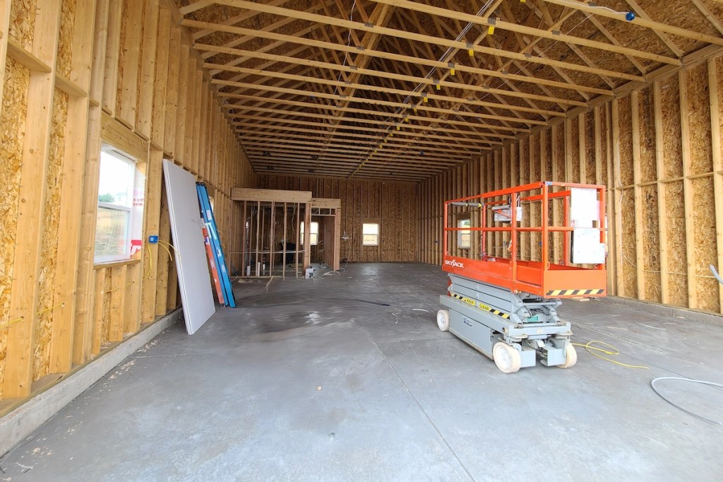 Interior of a large detached garage under construction showing electrical rough-in wiring and scissor lift